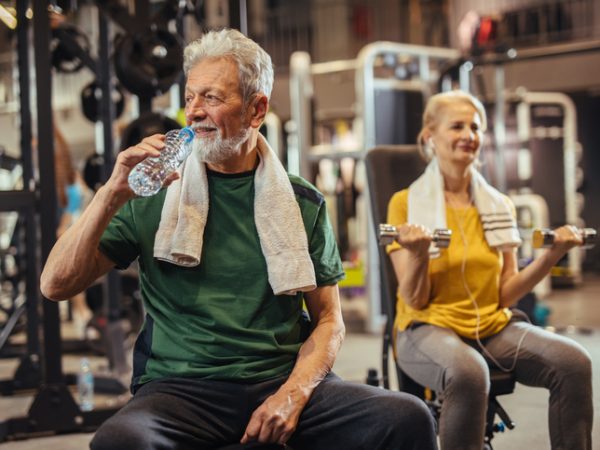 Senior man drinking water and taking a break from his workout at the gym