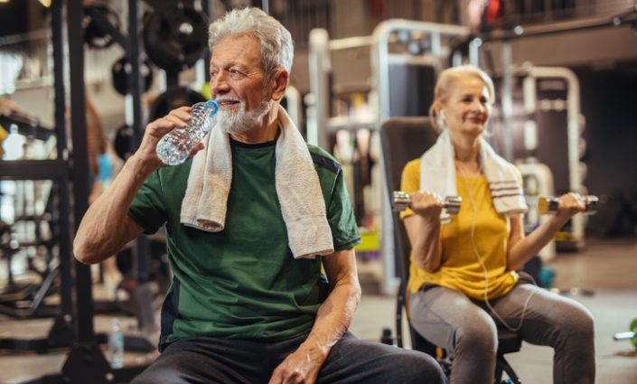 Senior man drinking water and taking a break from his workout at the gym